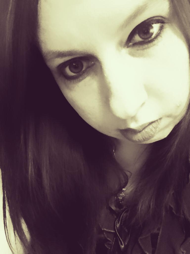 Portret kobiety z ciemnymi włosami, patrzącej w dół z intensywnym spojrzeniem, w sepii.