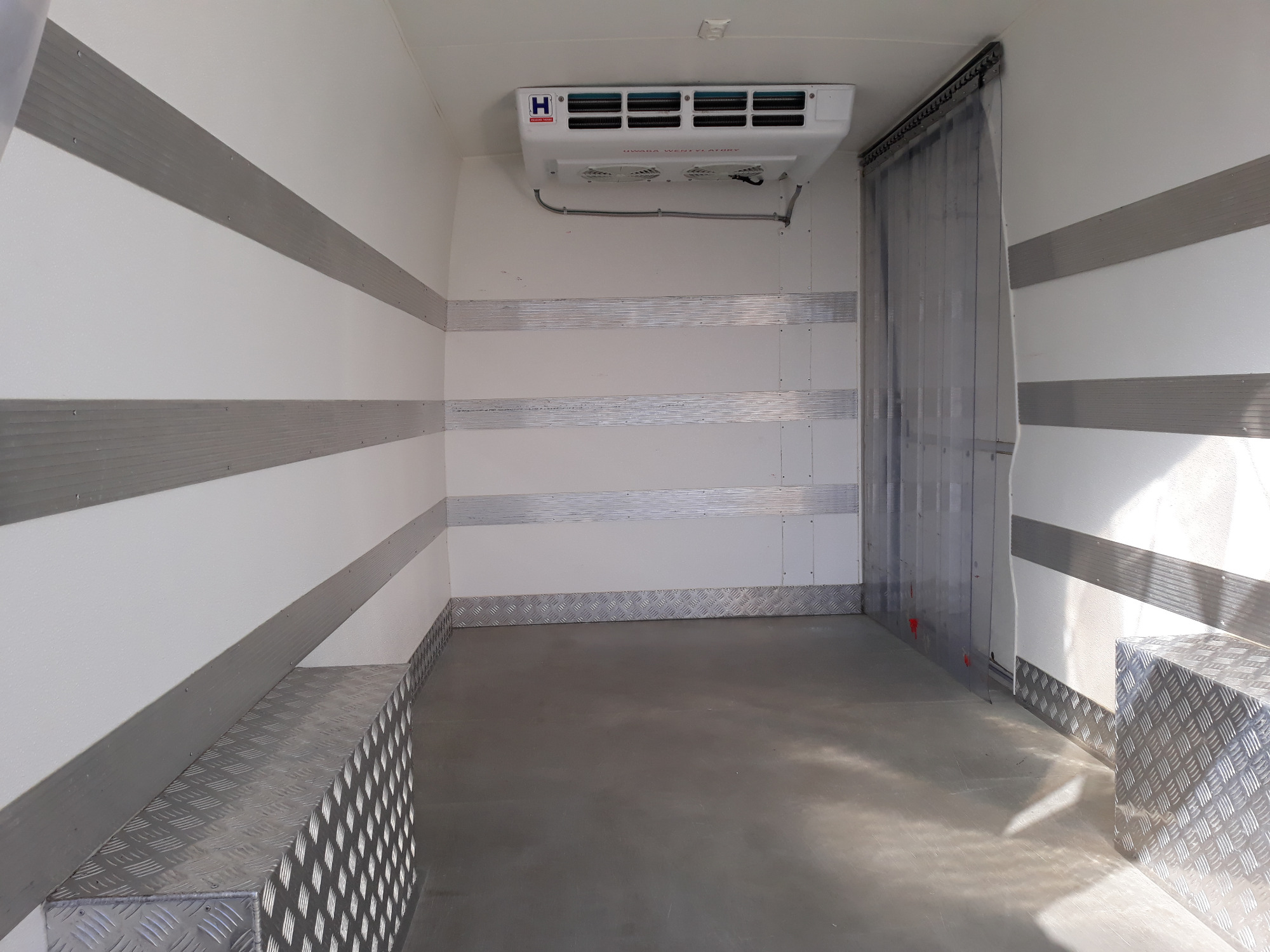 Wnętrze chłodni transportowej z aluminiowymi zabezpieczeniami ścian, agregatem chłodniczym i kurtyną paskową.