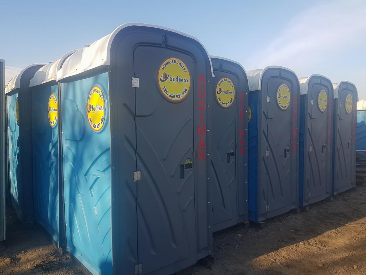 Rząd przenośnych toalet w kolorach niebieskim i szarym, ustawionych na ziemi, z widocznym logo firmy 'budimax' i numerem telefonu.