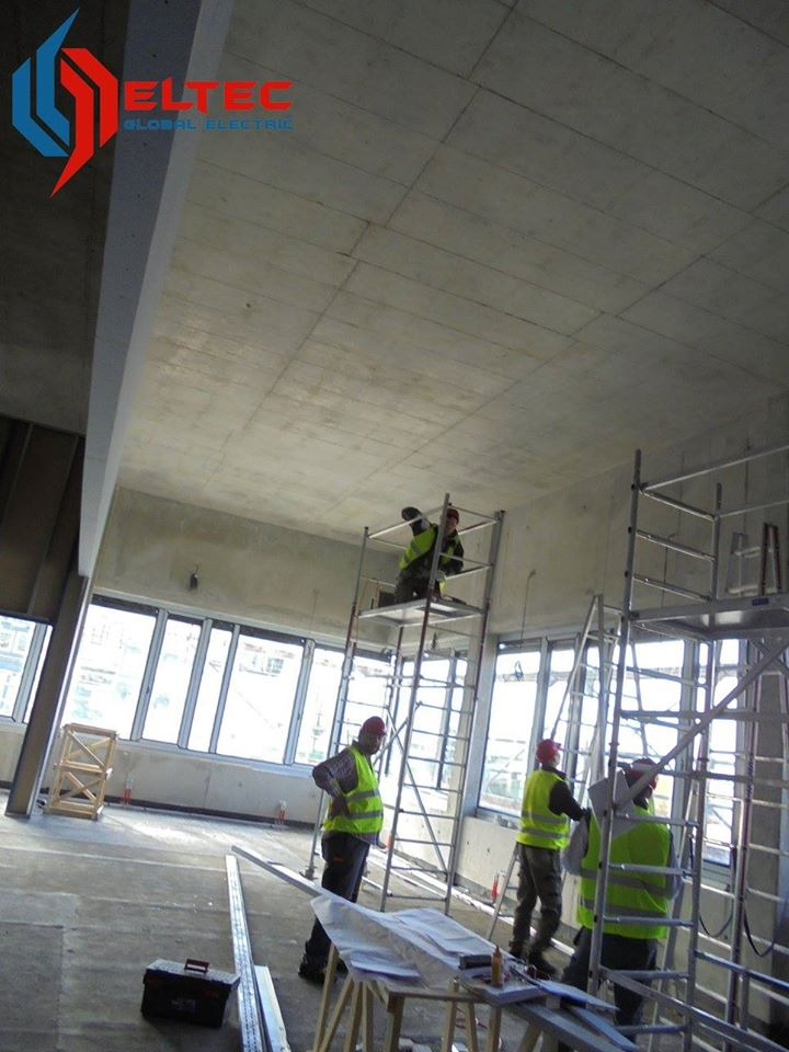 Prace instalacyjne w surowym wnętrzu budynku w Jaworznie. Elektrycy na rusztowaniach montują instalacje pod sufitem. Widoczne narzędzia i materiały budowlane.