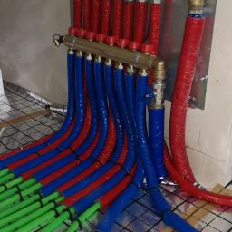 Termomik Mariusz Mikowski - Rozdzielacz ogrzewania podłogowego z rurami w kolorach: czerwonym, niebieskim i zielonym, ułożonymi na folii izolacyjnej z nadrukowaną siatką.