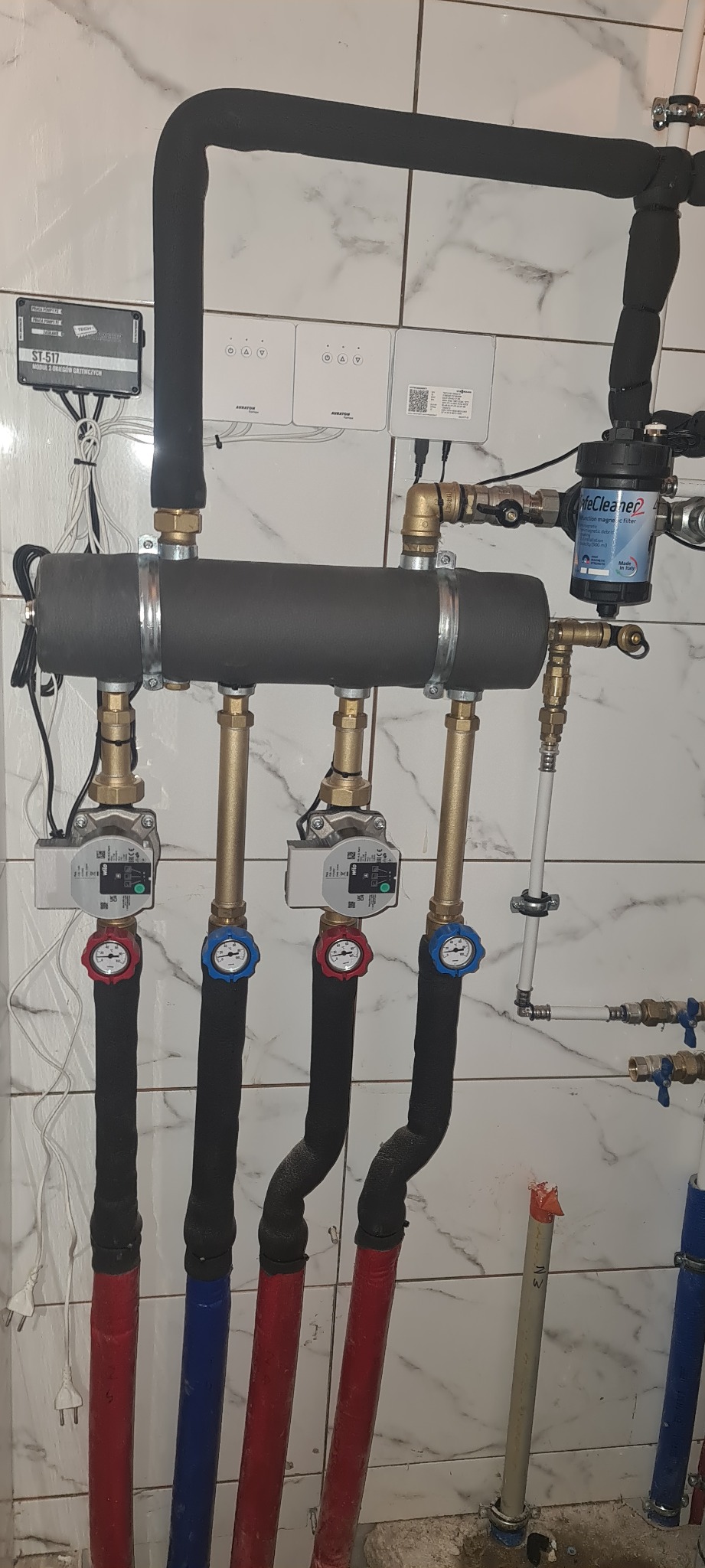 Rozdzielacz instalacji grzewczej z czterema obiegami, każdy z pompą obiegową i termometrem, rury w izolacji, filtr magnetyczny SafeCleaner2, moduł sterujący ST-517 i dwa panele sterowania Auraton.