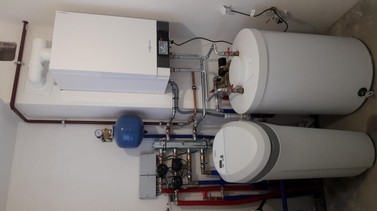 Kompletna instalacja kotła grzewczego Viessmann z dwoma zbiornikami na wodę, niebieskim naczyniem przeponowym i licznymi rurami miedzianymi i plastikowymi w schludnym pomieszczeniu technicznym.