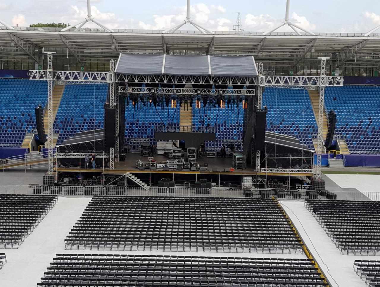 Scena koncertowa w trakcie montażu na stadionie: metalowa konstrukcja, oświetlenie, nagłośnienie, krzesła dla publiczności, widok z góry.