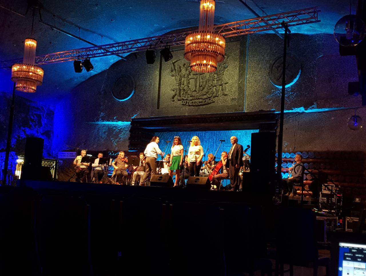 Występ zespołu muzycznego i wokalistów na scenie w kopalni soli z oświetleniem scenicznym i żyrandolami