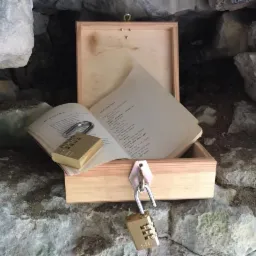 Drewniana skrzynka z otwartą książką i dwoma kłódkami szyfrowymi w kamiennej grocie, element gry typu escape room