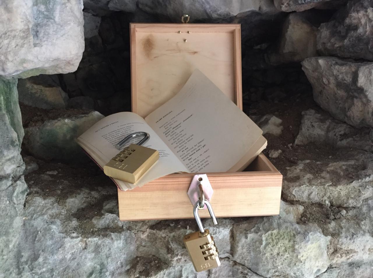 Drewniana skrzynka z otwartą książką i dwoma kłódkami szyfrowymi w kamiennej grocie, element gry typu escape room