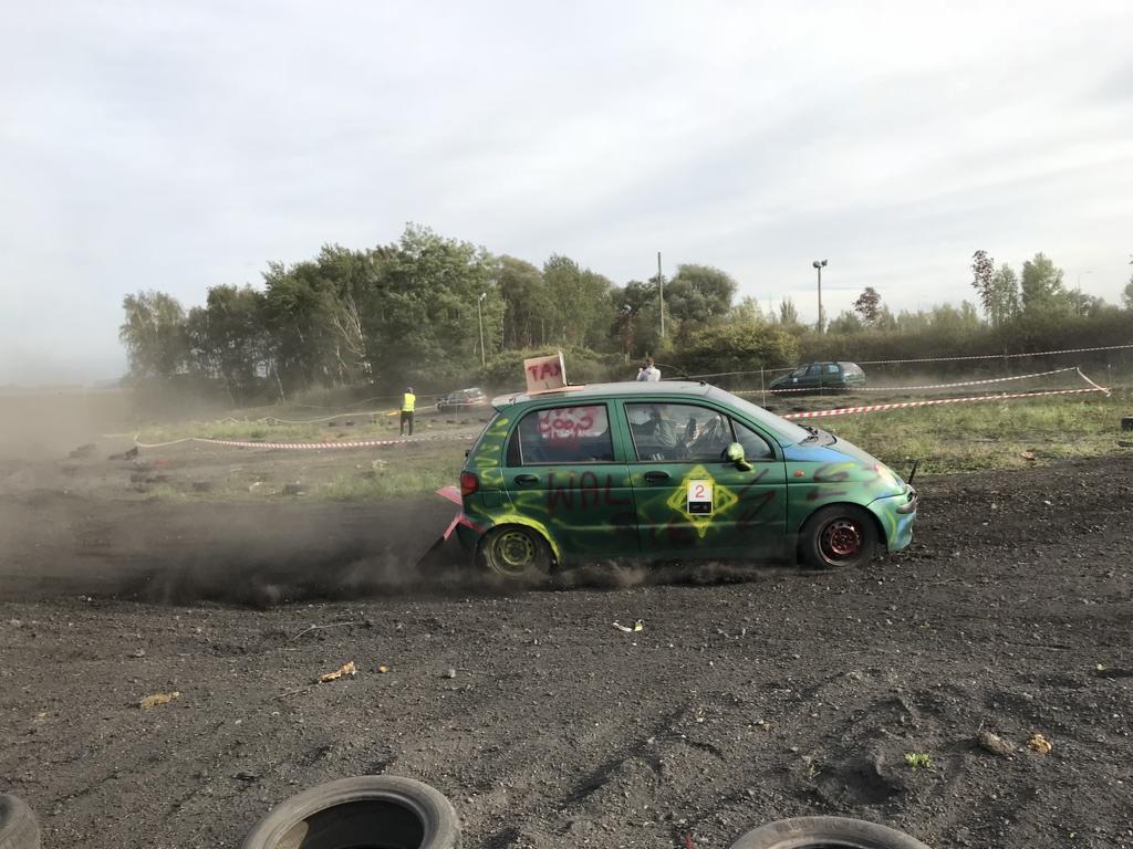 Zielony, pomalowany samochód z numerem 2 wjeżdża w chmurę kurzu na błotnistym torze podczas wyścigu w terenie.