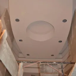 Sufit podwieszany z okrągłym wgłębieniem i otworami na oświetlenie punktowe, widok z rusztowania podczas prac.