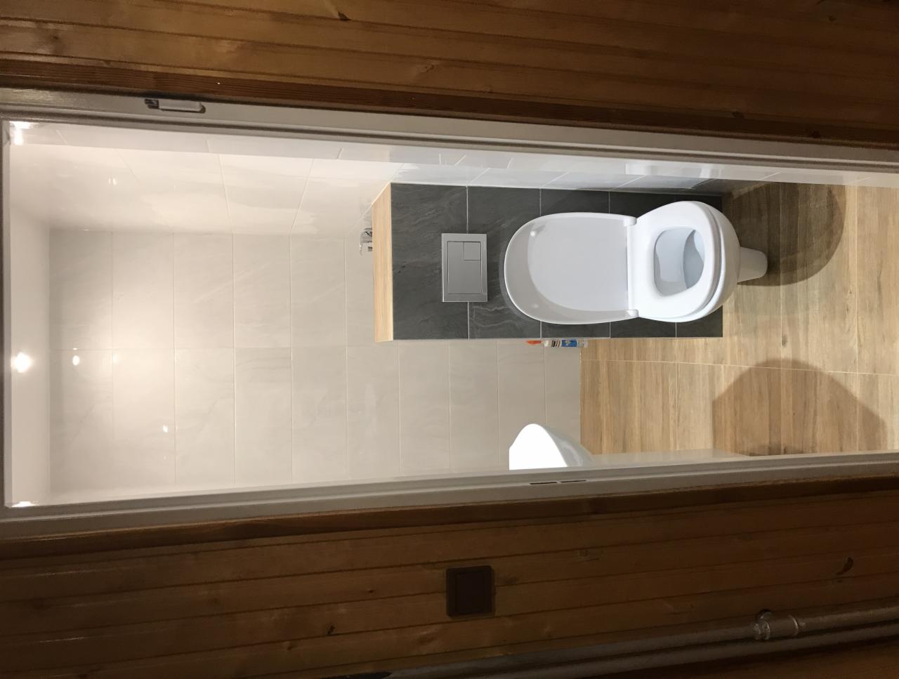 Widok z góry na wykończoną łazienkę z drewnianymi ścianami, z białą toaletą i szarymi oraz drewnopodobnymi płytkami na ścianach i podłodze.