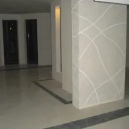 Wykończony filar z dekoracyjnymi, jasnymi liniami na szarej powierzchni, widoczny w przestronnym holu z błyszczącą podłogą i małym dzieckiem stojącym w oddali.