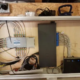 Rozdzielnica antenowa Terra z podłączonymi kablami koncentrycznymi i patch panelem TP-Link z kablami sieciowymi, router Huawei, zainstalowane w drewnianej obudowie, widoczne gniazdka elektryczne...