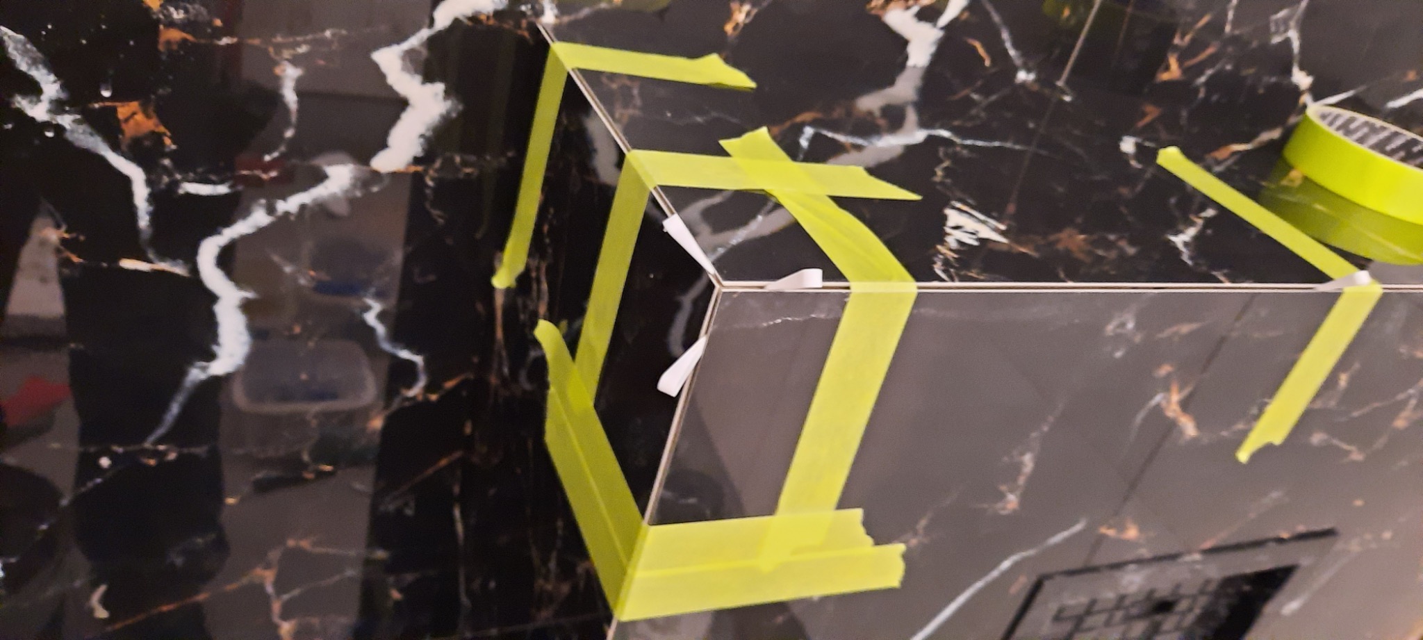 Układanie płytek imitujących marmur na narożniku, zabezpieczonych żółtą taśmą malarską.