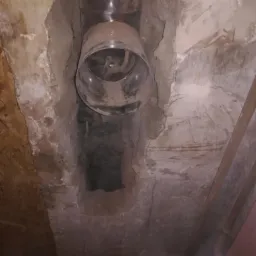 Metalowy wkład kominowy zamontowany w starym, częściowo rozkruszonym kominie murowanym, widoczne ślady sadzy i pyłu.