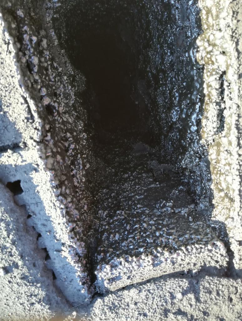 Wnętrze komina z widocznymi osadami smoły i sadzy na ścianach, oświetlone z góry.