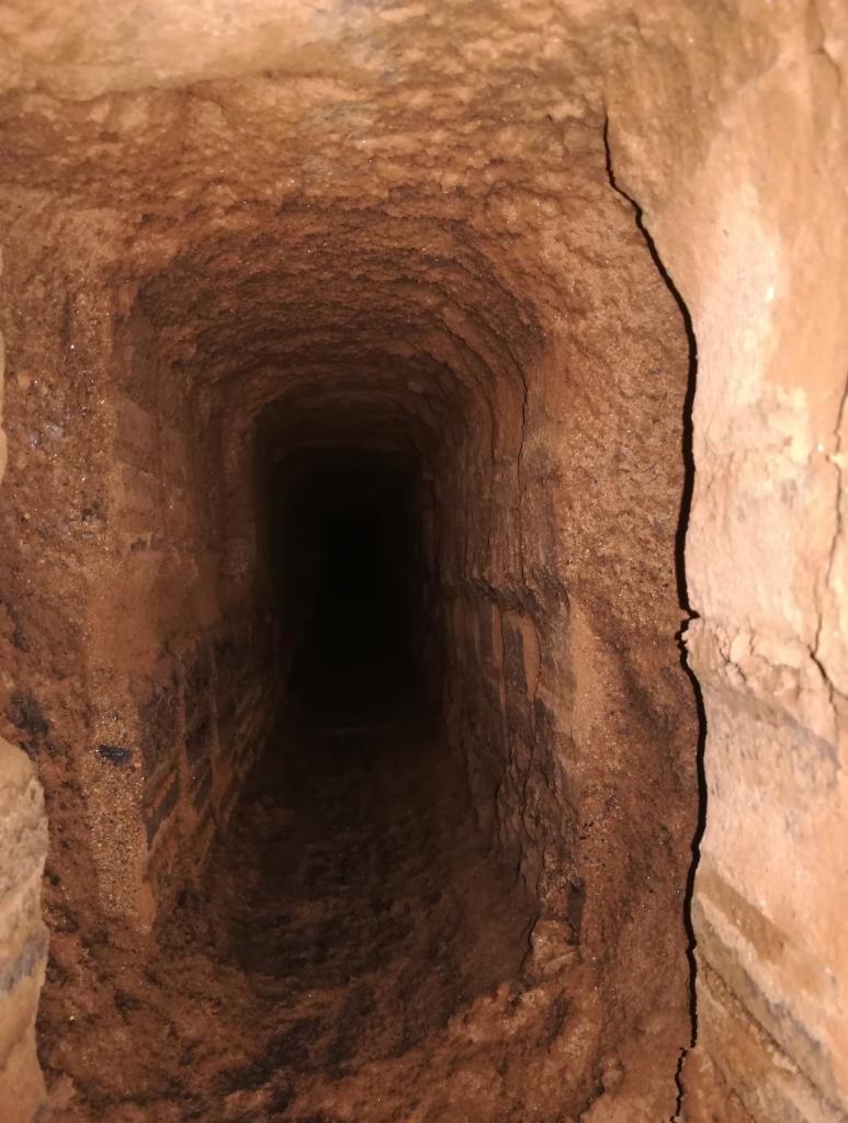 Wnętrze ceglanego przewodu kominowego z widocznymi śladami sadzy i zabrudzeń, skierowane w głąb ciemności.