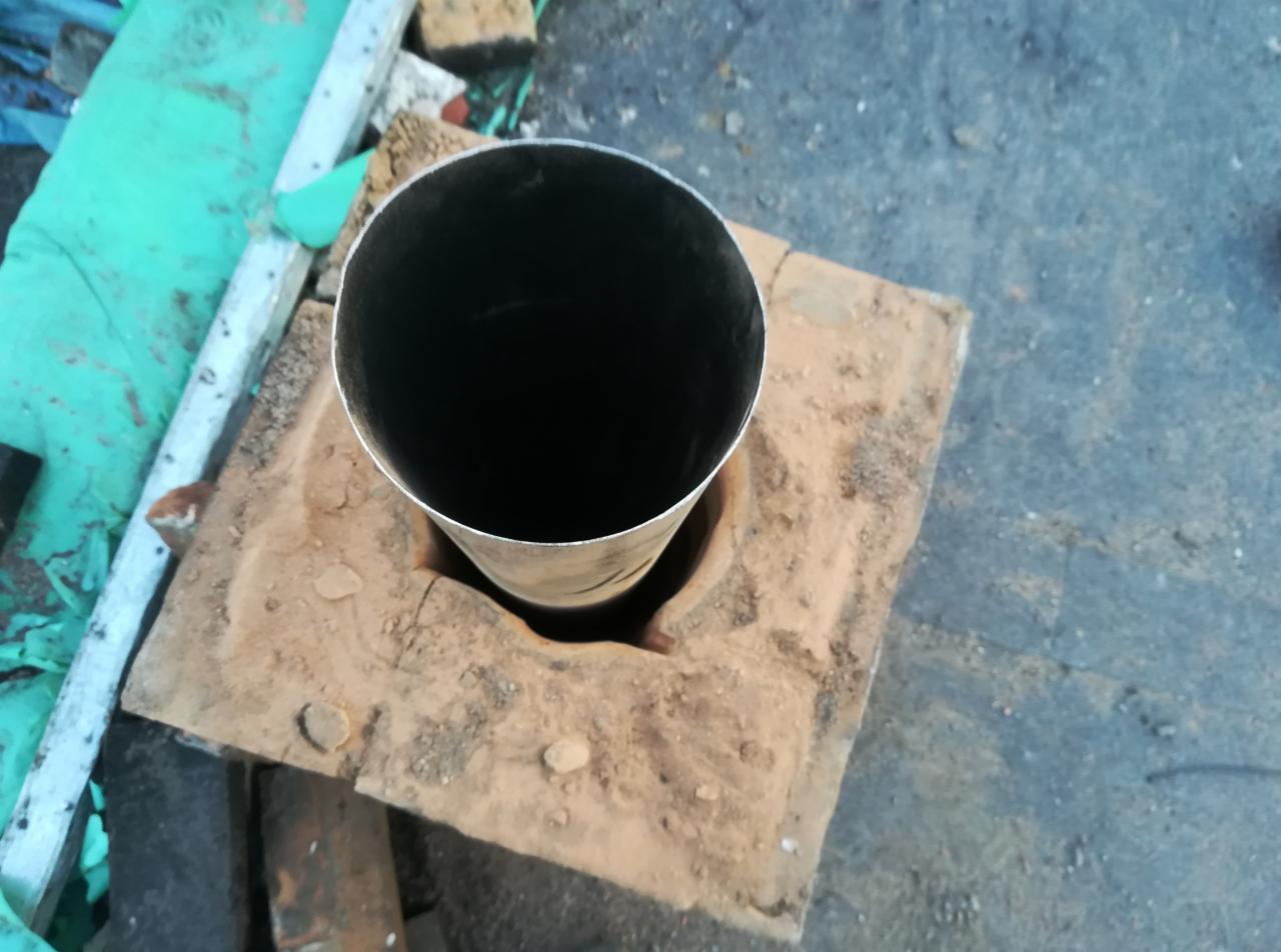 Metalowa rura kominowa wystająca z ceglanej podstawy, widok z góry, otoczenie budowlane.