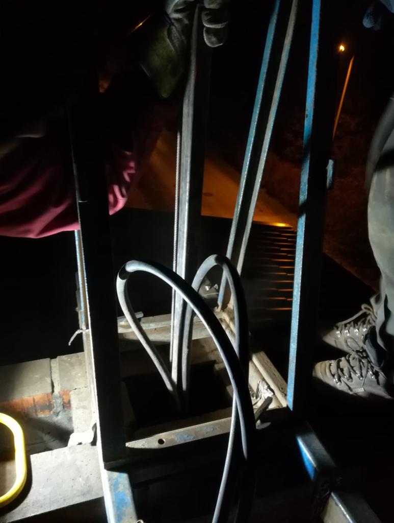 Wnętrze komina z widocznymi elementami konstrukcyjnymi, narzędziami i fragmentem osoby w roboczych butach, oświetlone z góry.