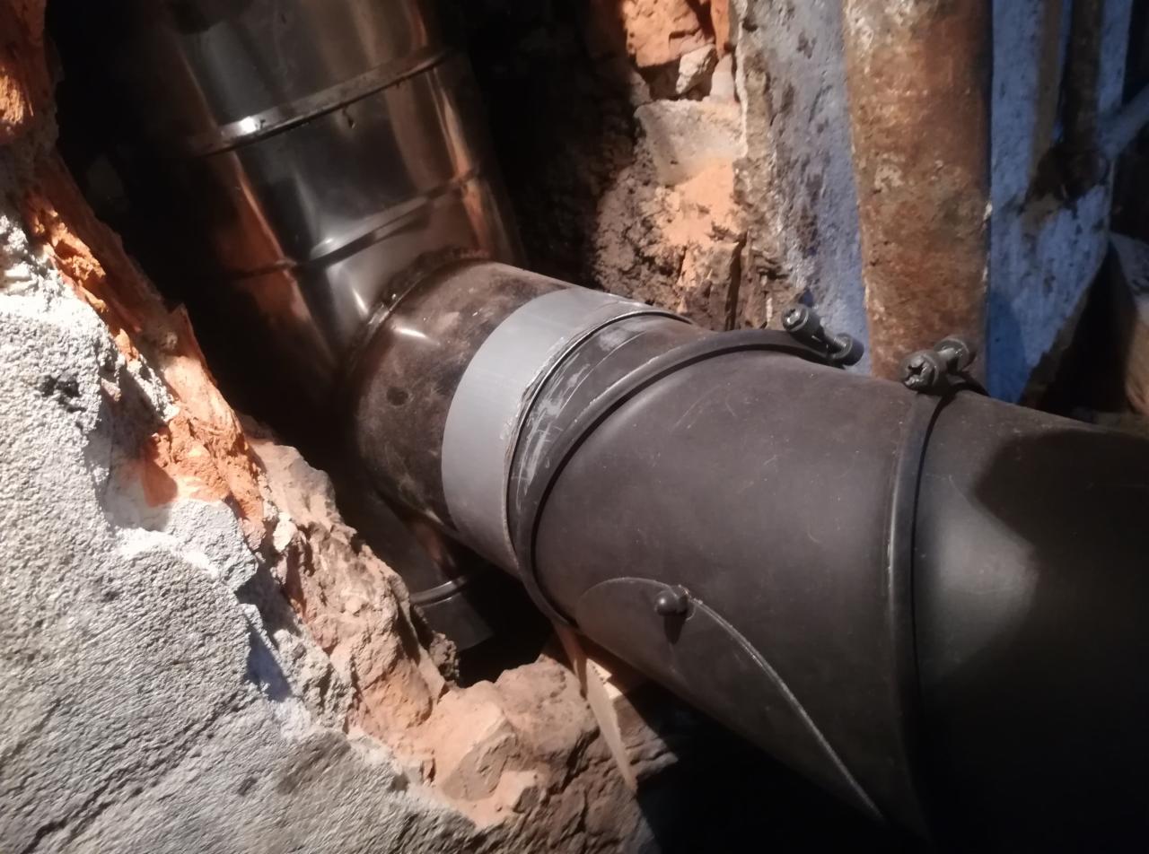 Połączenie rur dymowych w kominie z widocznym fragmentem ceglanej ściany i zaprawy