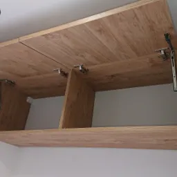 Otwarta szafka wisząca z drewnopodobnymi frontami i metalowymi podnośnikami gazowymi, zamontowana w Grodzisku Mazowieckim.