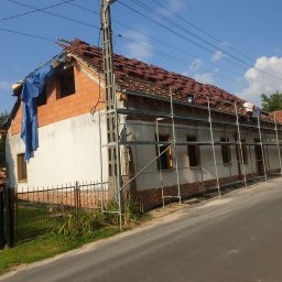 Rafał Jastrzębski - Dom w trakcie wymiany dachu z częściowo ułożoną dachówką, zabezpieczony niebieską plandeką, z widocznym rusztowaniem i pracownikami na dachu, Toszek.