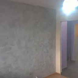 Ściana z efektem dekoracyjnym w odcieniach szarości, wykonana w mieszkaniu w Miechowie, widoczna z perspektywy podłogi, z widocznym przejściem do innego pomieszczenia z fioletowymi ścianami.