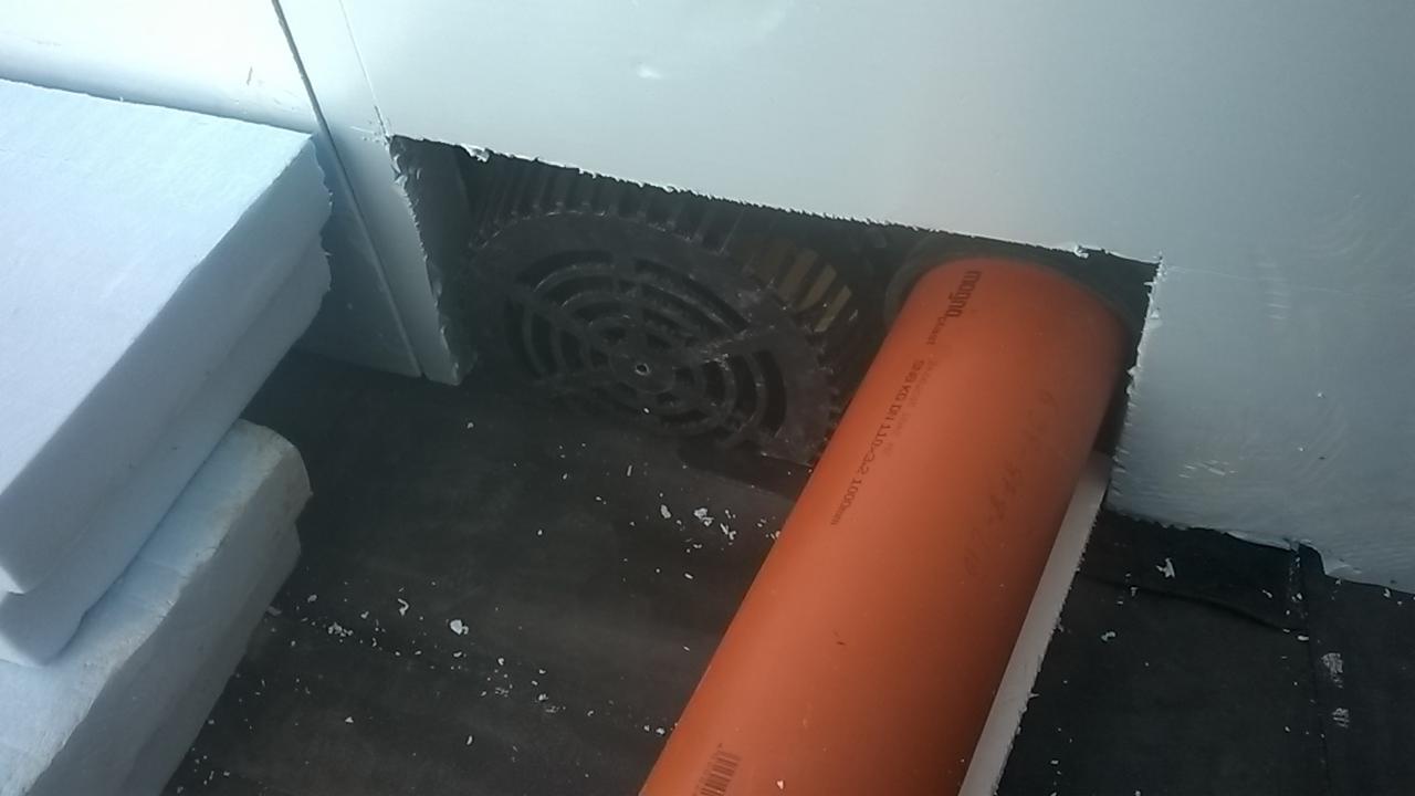 Fragment poddasza w trakcie ocieplania: widoczna warstwa izolacji ze styropianu, pomarańczowa rura wentylacyjna oraz kratka wentylacyjna w ścianie.