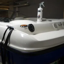 Biała motorówka z niebieskim pasem, z butelką środka czyszczącego na pokładzie, widoczne detale takie jak knaga cumownicza, wlew paliwa i silnik MerCruiser.