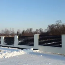 Nowoczesne ogrodzenie panelowe z czarnymi przęsłami i białymi słupkami w zimowym krajobrazie.