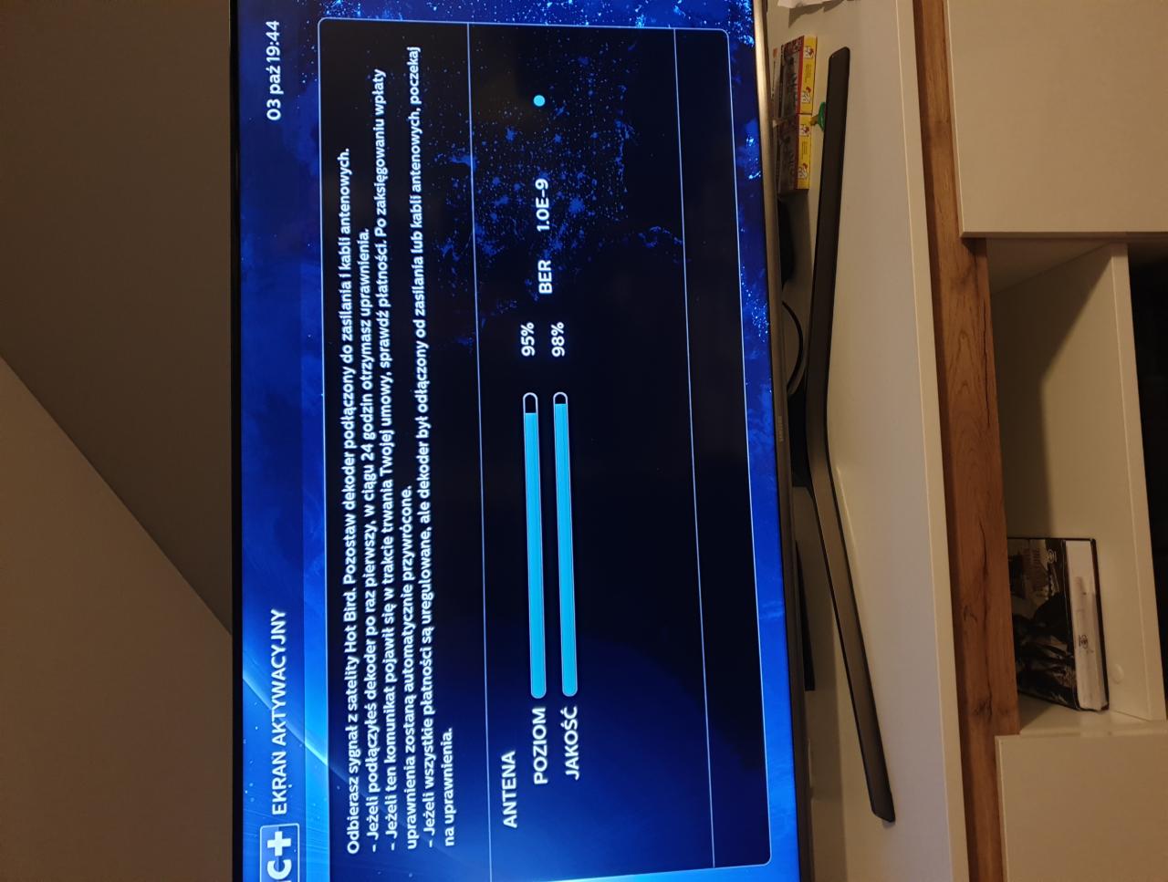 Ekran telewizora wyświetlający informacje o aktywacji dekodera satelitarnego, z widocznymi wskaźnikami poziomu i jakości sygnału antenowego oraz instrukcjami dotyczącymi podłączenia i uprawnień.