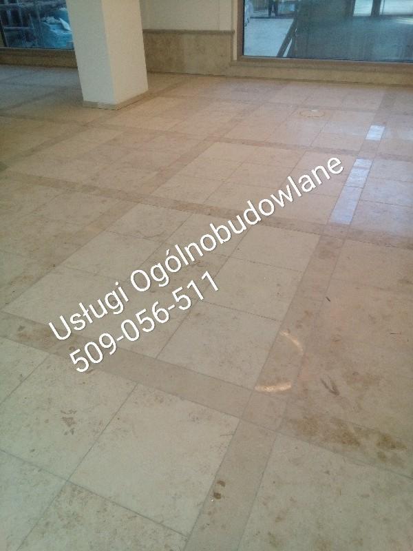 Wykończona podłoga z jasnego kamienia w Bolesławcu, z widocznym słupem i oknem w tle. Na podłodze widnieje napis 'Usługi Ogólnobudowlane 509-056-511'.