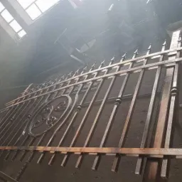 Metalowa brama z dekoracyjnym ornamentem w trakcie obróbki, widoczna w hali warsztatowej przy świetle dziennym z okna