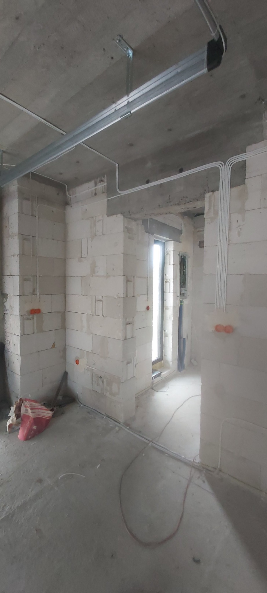 Surowy stan wnętrza z białymi ścianami z betonu komórkowego, widoczne kable elektryczne poprowadzone po ścianach i pod sufitem, puszki instalacyjne zamontowane w ścianach, brak wykończenia podłogi.