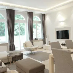 Jasny salon z trzema wysokimi oknami łukowymi z szarymi zasłonami, beżową sofą modułową, obrotowym fotelem, stolikiem kawowym i stołem jadalnym z szarymi krzesłami.