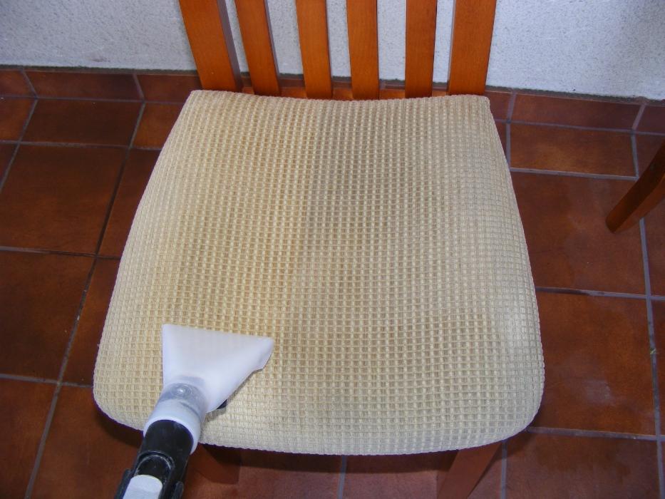 Czyszczenie beżowego krzesła tapicerowanego z widoczną końcówką odkurzacza piorącego i brązową podłogą z płytek w tle.