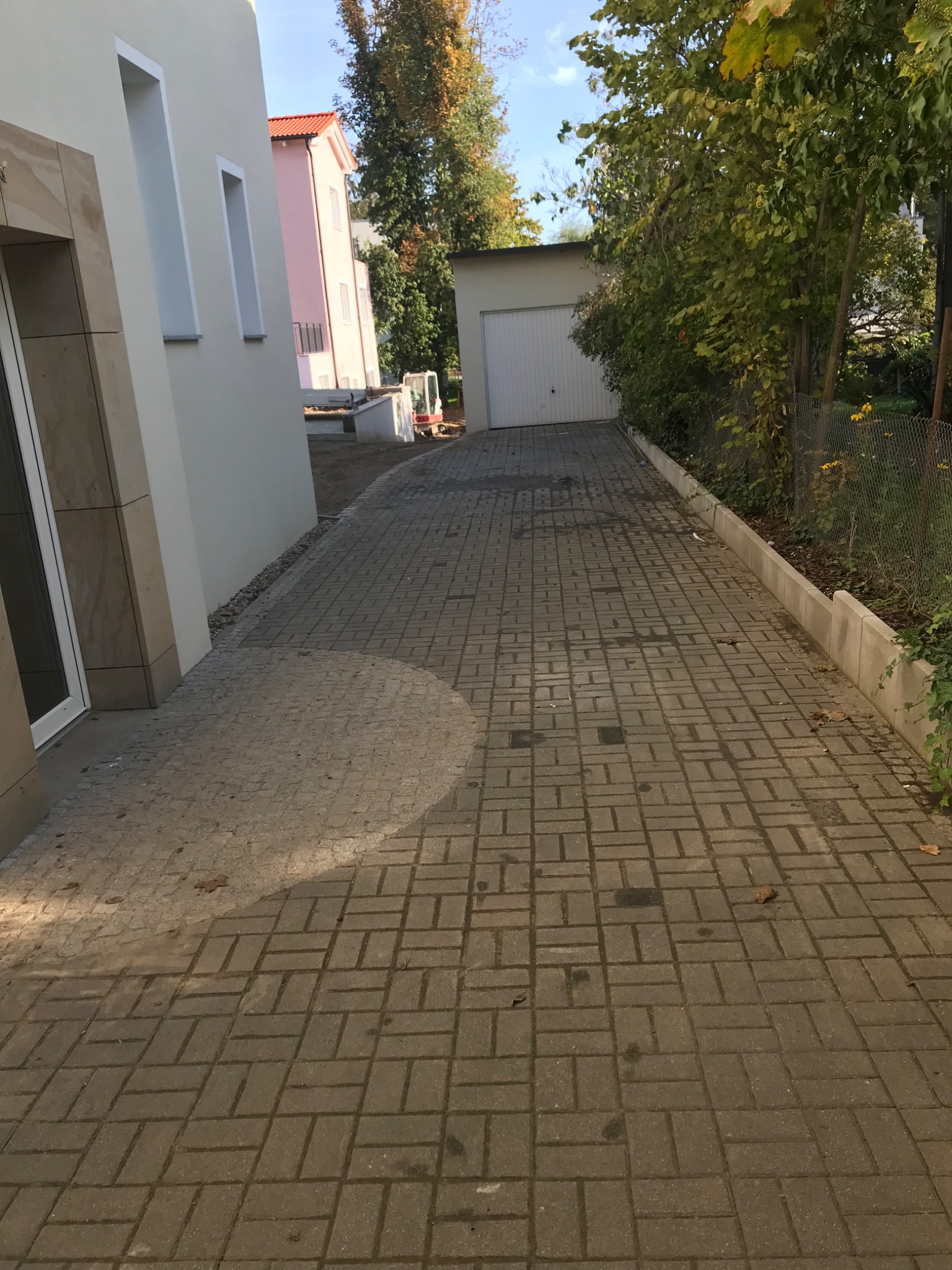 Ułożona szara kostka brukowa w kształcie prostokątów tworząca podjazd do garażu, z widocznym fragmentem budynku i ogrodu w tle.