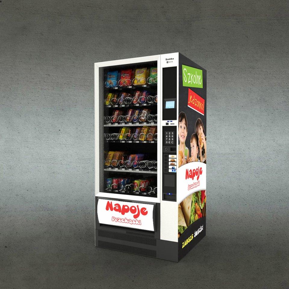 Automat vendingowy Samba z przekąskami i napojami, z grafiką 'Szkolne Jedzonko' i zdjęciem dzieci, ustawiony na tle szarej ściany.