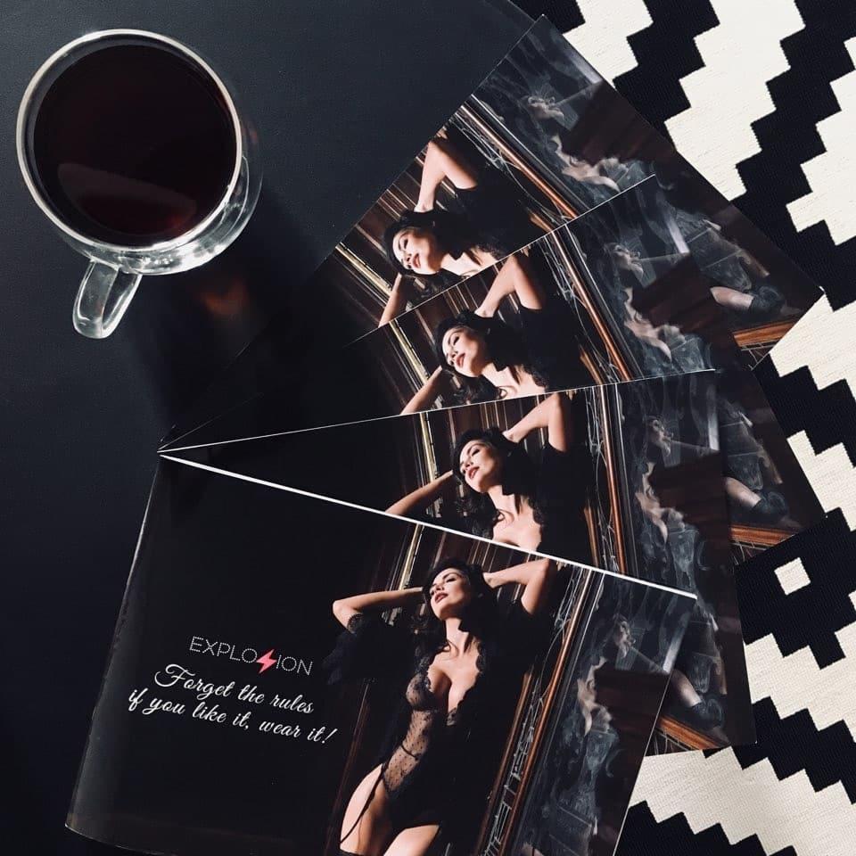 Ułożone pod kątem ulotki reklamowe z sesją zdjęciową modelki w bieliźnie, obok filiżanka kawy i fragment czarno-białego dywanu, Bydgoszcz.