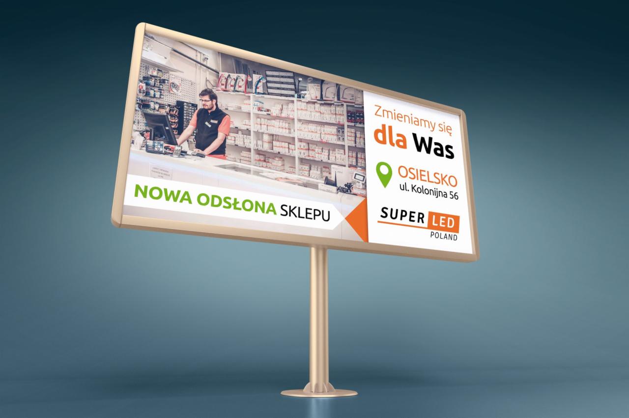 Billboard reklamujący nową odsłonę sklepu z oświetleniem, widoczny pracownik za ladą i półki z produktami w tle.