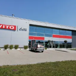 Budynek firmy Vito Okna w Siedlcach z zaparkowanym samochodem dostawczym z reklamą usług. Widoczne duże okna i logo firmy na elewacji.