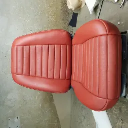 Odrestaurowane, czerwone skórzane siedzenie samochodowe z pionowymi przeszyciami, widoczne narzędzia tapicerskie w tle.