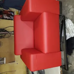 Czerwony, modułowy narożnik obity nową skórą ekologiczną, widoczny z góry, w tle warsztat z przewodami i narzędziami.