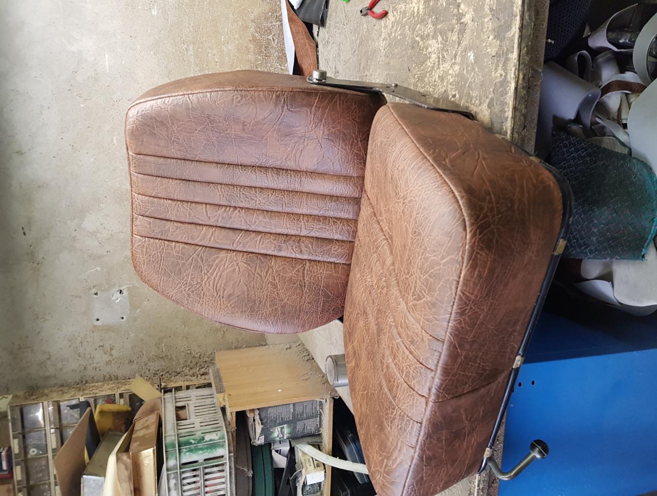 Dwa brązowe fotele samochodowe z nową skórzaną tapicerką, widoczne na tle warsztatu w Krosinku, z narzędziami i materiałami.