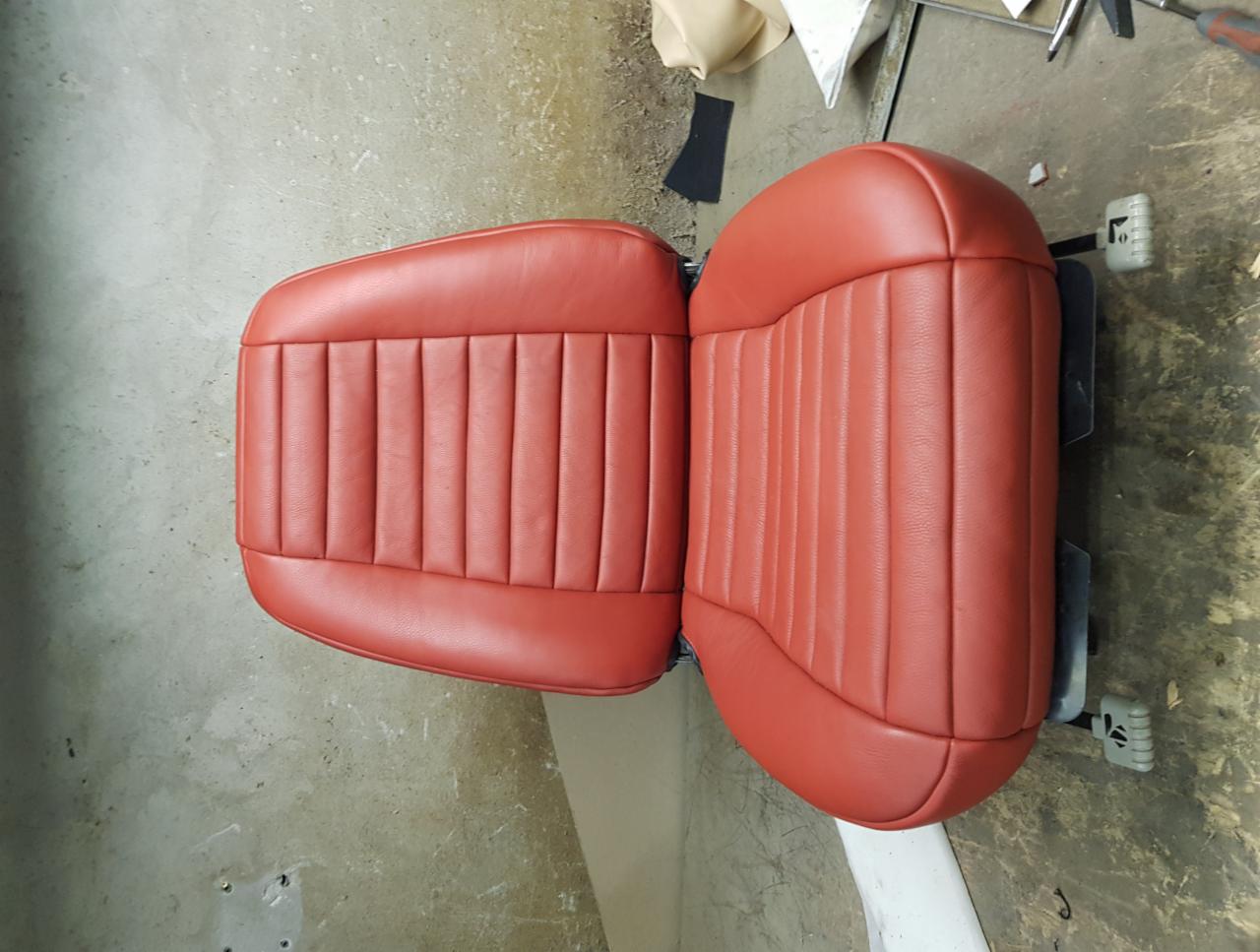 Odrestaurowane, czerwone skórzane siedzenie samochodowe z pionowymi przeszyciami, widoczne narzędzia tapicerskie w tle.