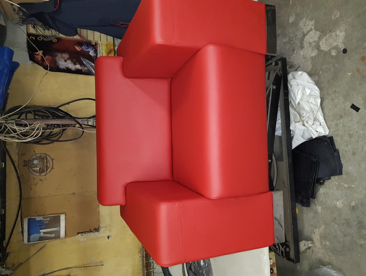 Czerwony, modułowy narożnik obity nową skórą ekologiczną, widoczny z góry, w tle warsztat z przewodami i narzędziami.