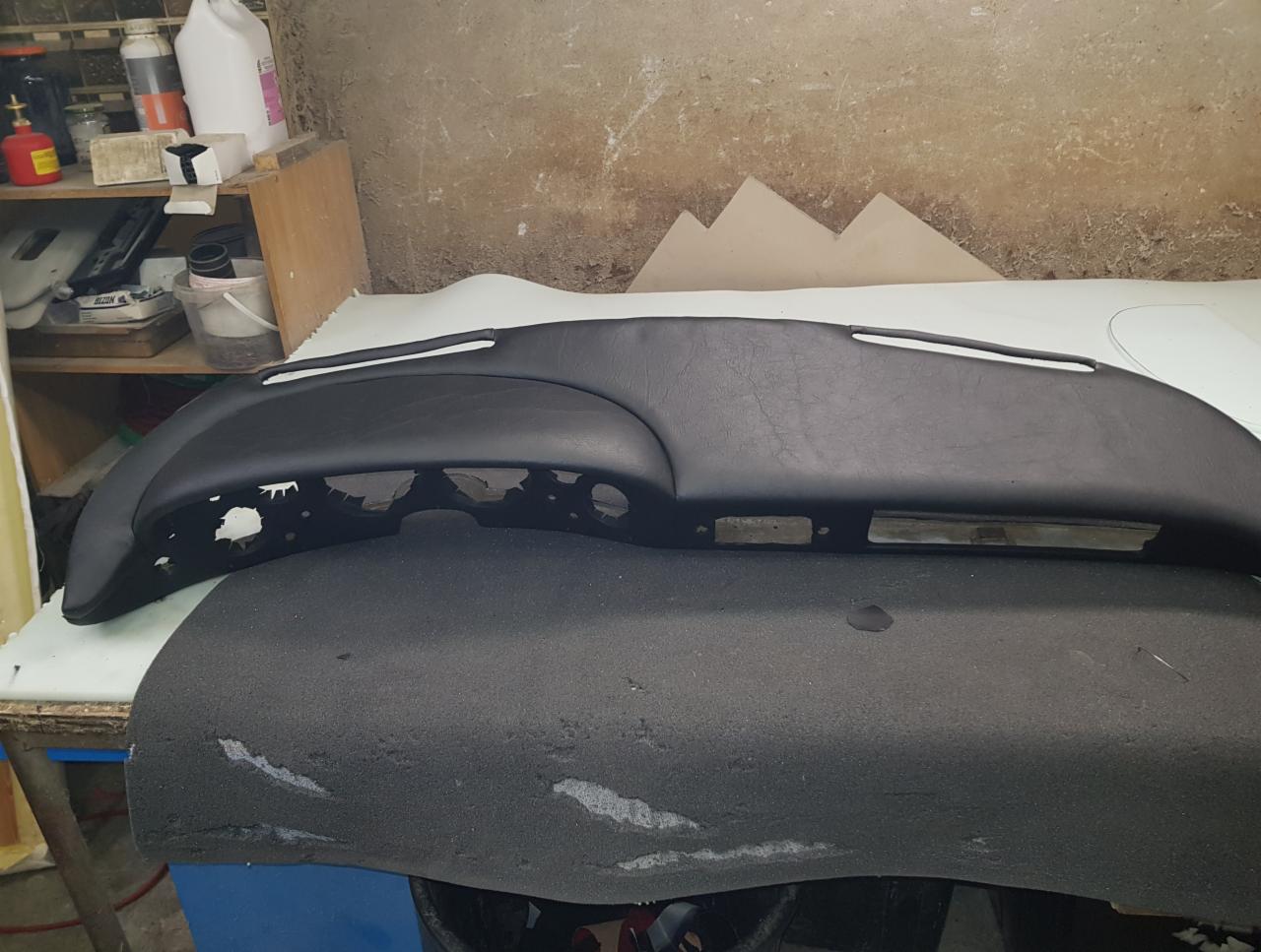 Czarny panel deski rozdzielczej samochodu, częściowo obity skórą, leżący na gąbce w warsztacie tapicerskim.