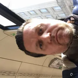 Mężczyzna robiący sobie selfie w pociągu, widoczne odbicie budynku w oknie.