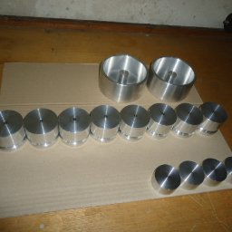 Usługi Tokarskie - Różne rozmiary i kształty metalowych elementów po obróbce, ułożone na kartonie na drewnianej podłodze.