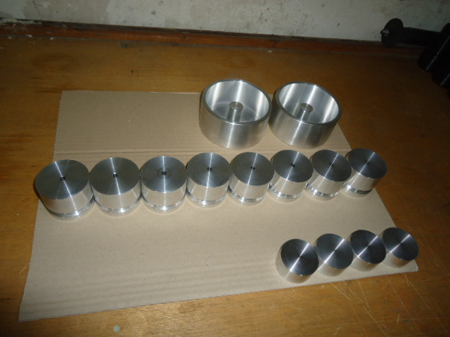 Różne rozmiary i kształty metalowych elementów po obróbce, ułożone na kartonie na drewnianej podłodze.