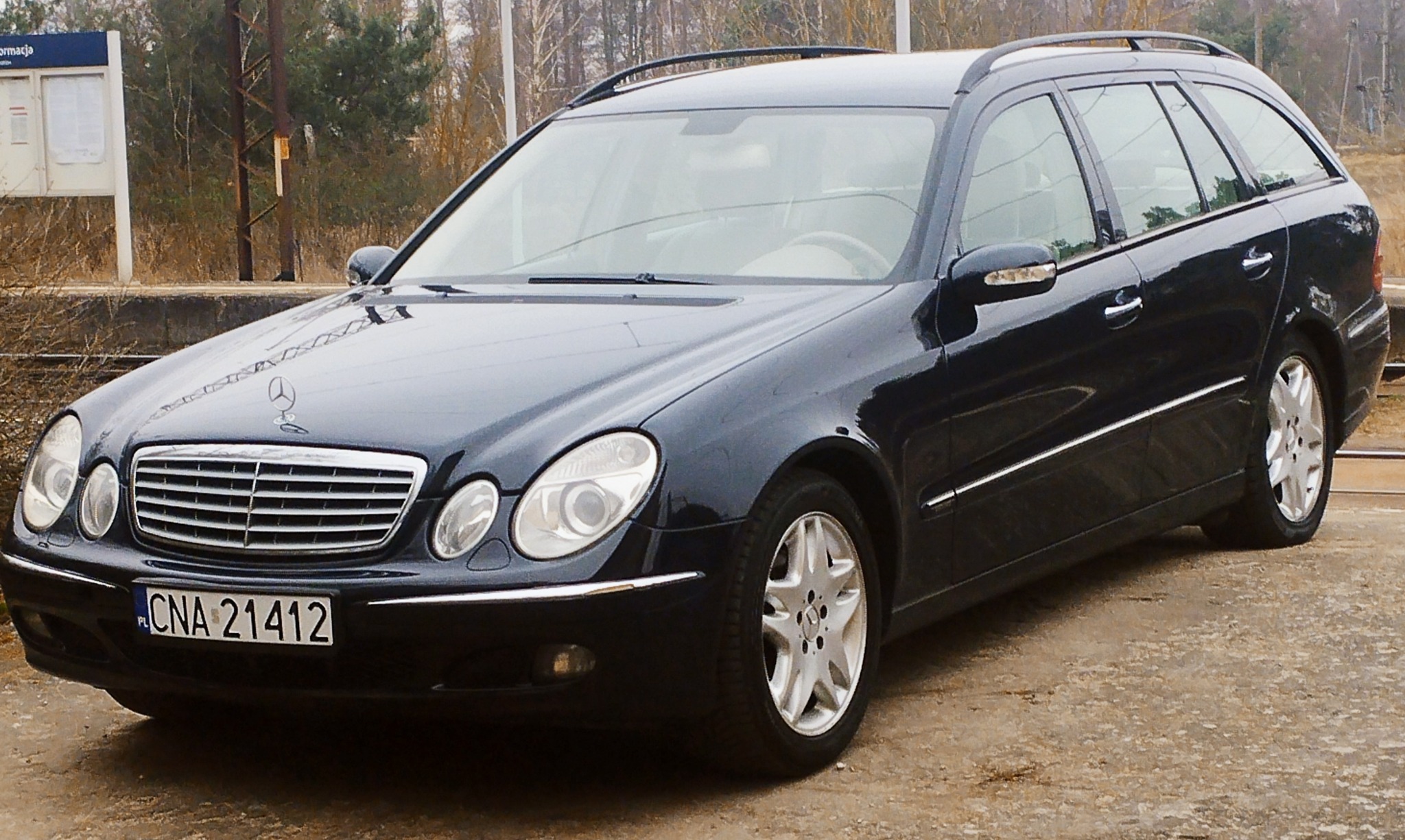 Czarny Mercedes-Benz kombi z polską rejestracją, zaparkowany w pobliżu peronu kolejowego, z widocznym znakiem firmowym na masce.